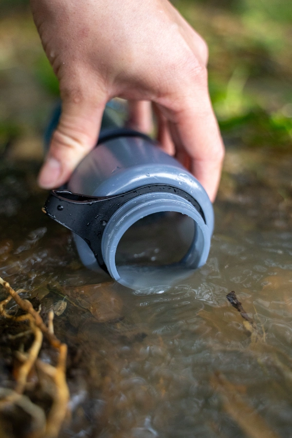 Waterfles met filter voor reizen wordt bijgevuld uit een rivier tijdens backpacken en outdoor avontuur